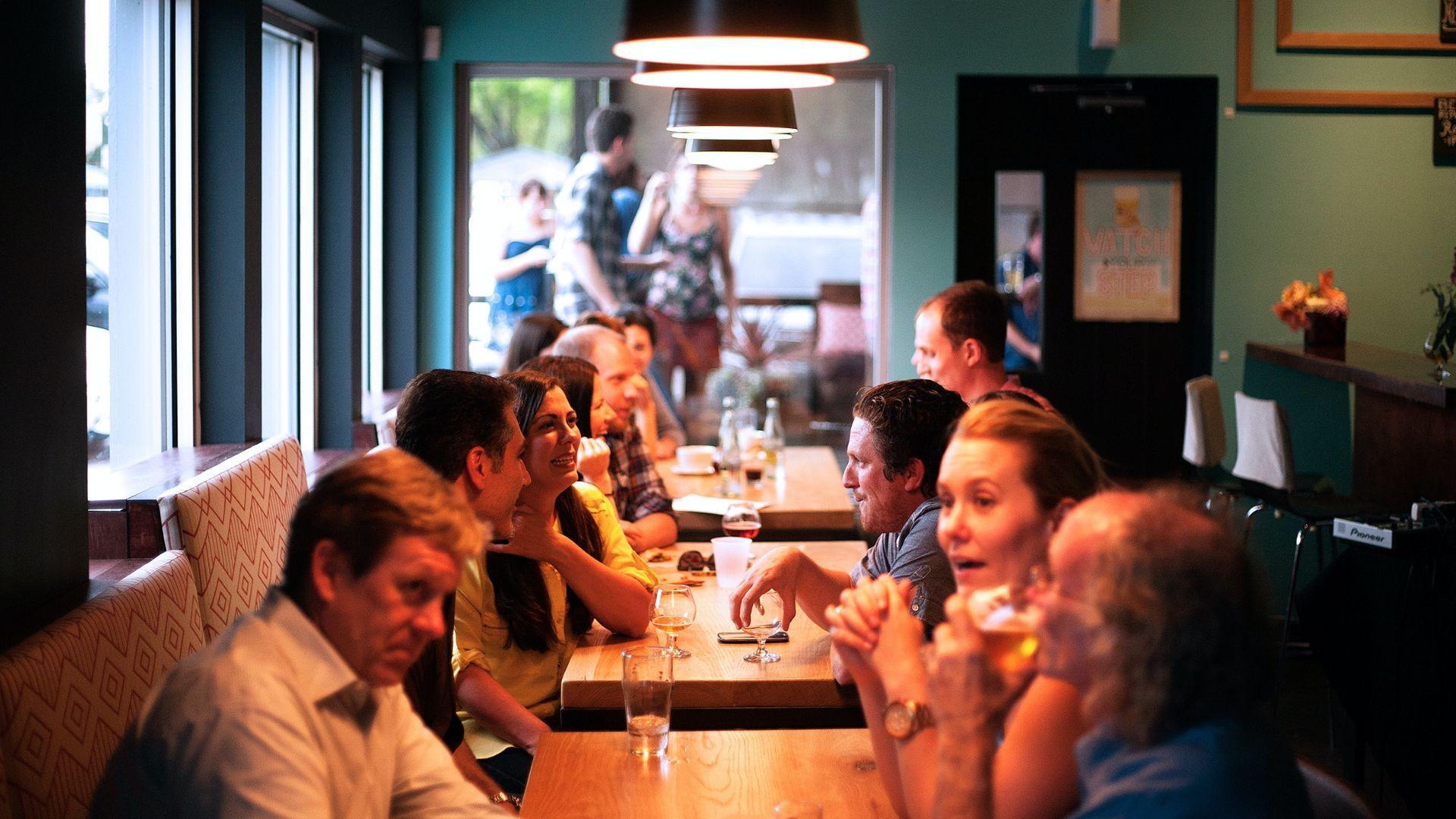 Groups of people seated at tables in a restaurant with teal-colored walls, engaging in conversations