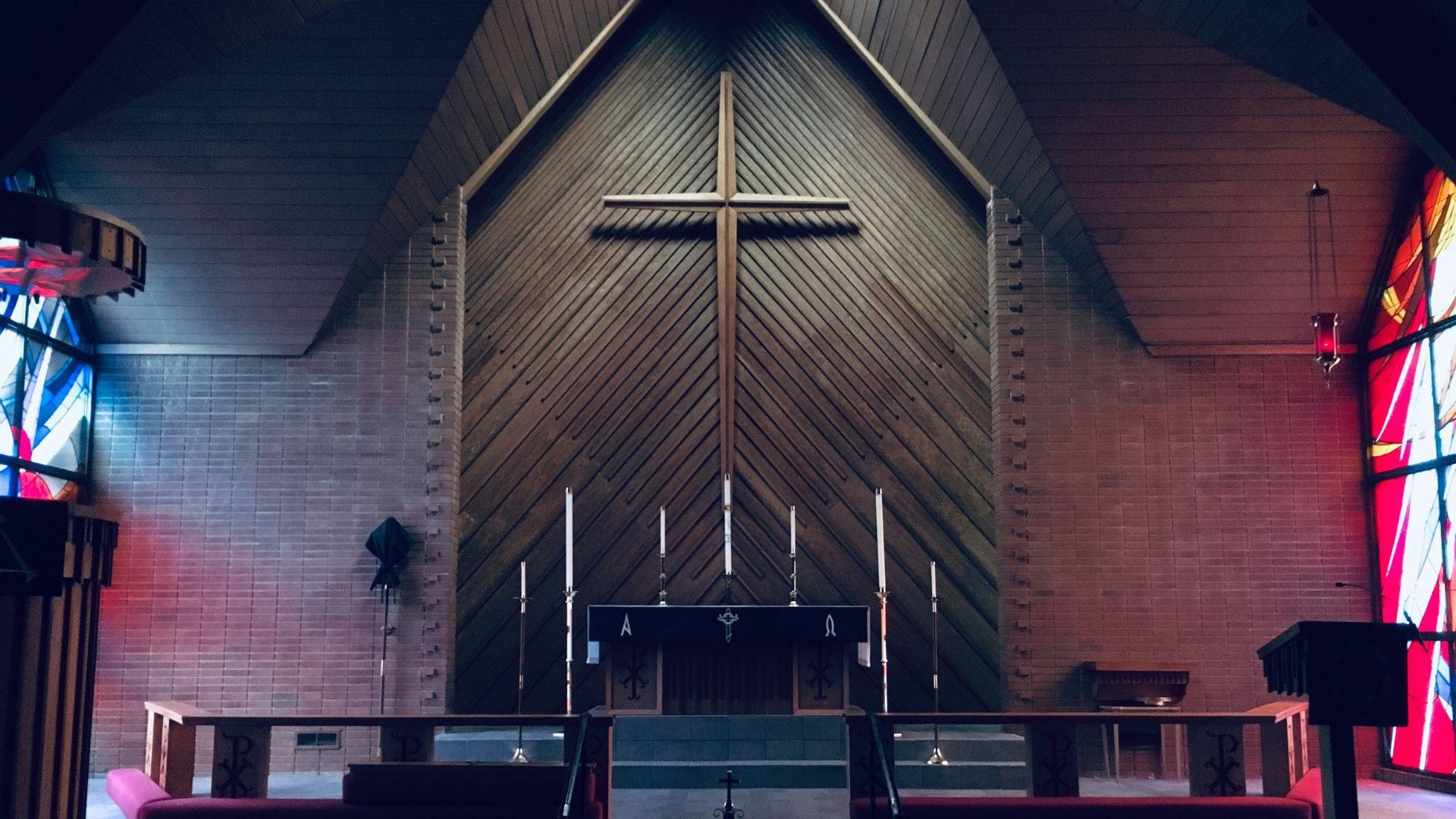 Interior of a church focused on the altar. The altar is centered beneath a large wooden cross mounted on a wooden-paneled wall