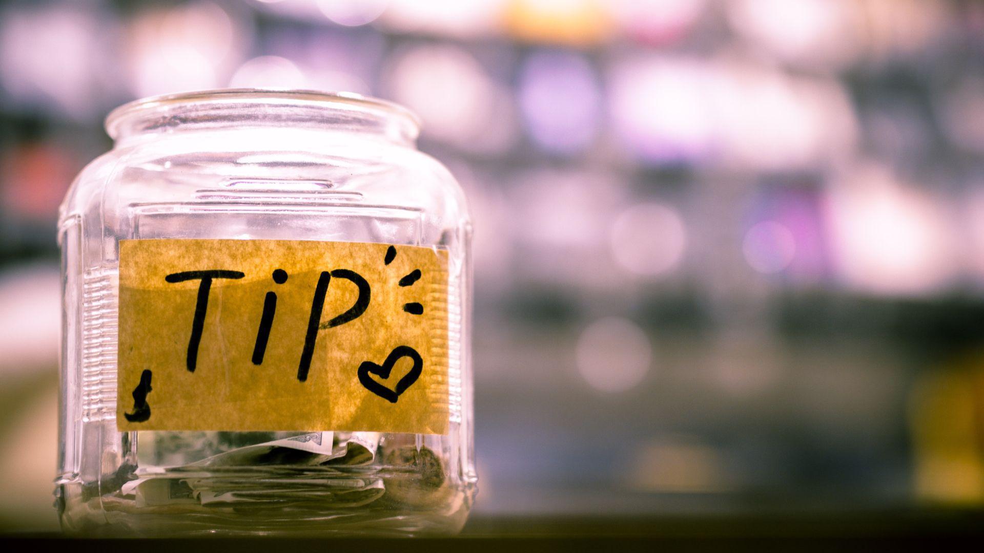 Clear glass jar labeled 'Tip' with a handwritten note and a heart symbol, containing some bills