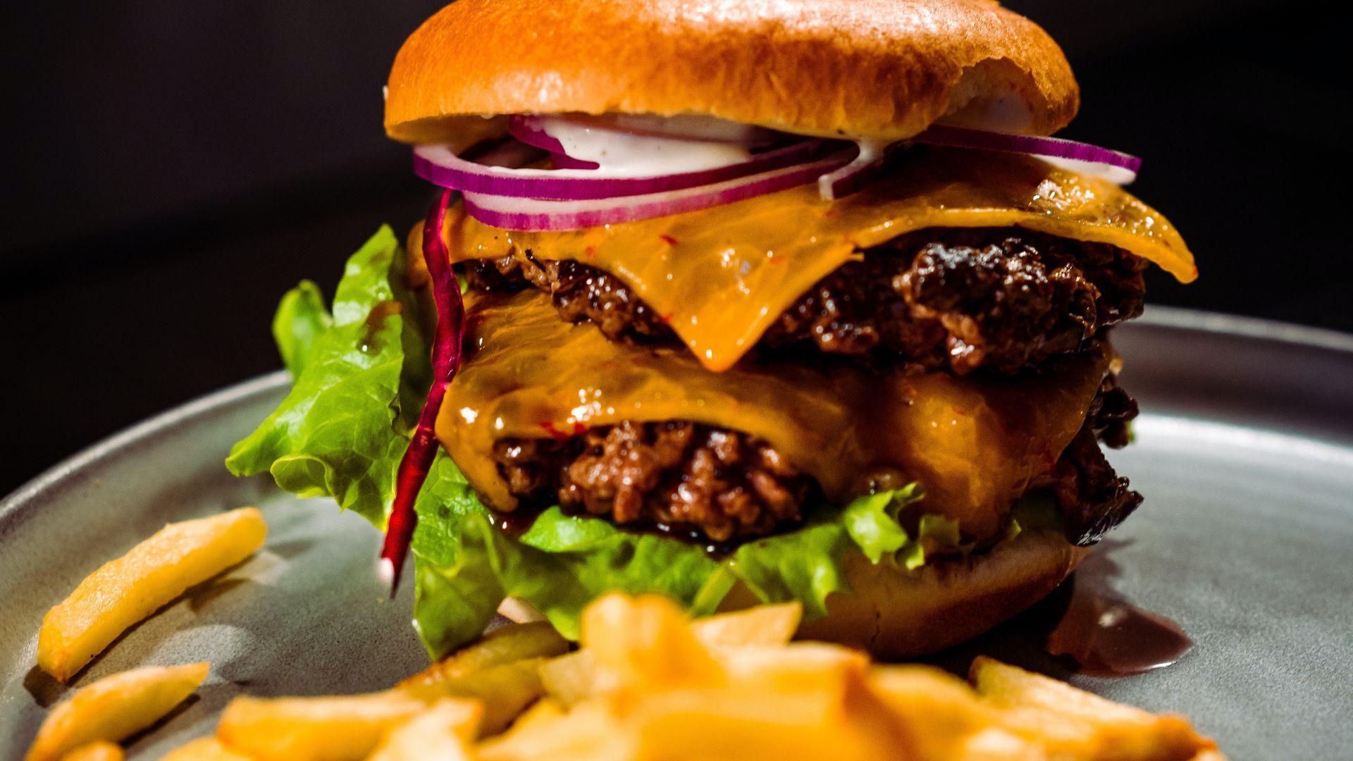 Detailed view of a large burger with melted cheese, lettuce, and sliced red onions on a bun, accompanied by a side of fries