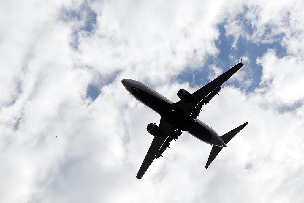 Airplane flies through the sky with clouds in the background